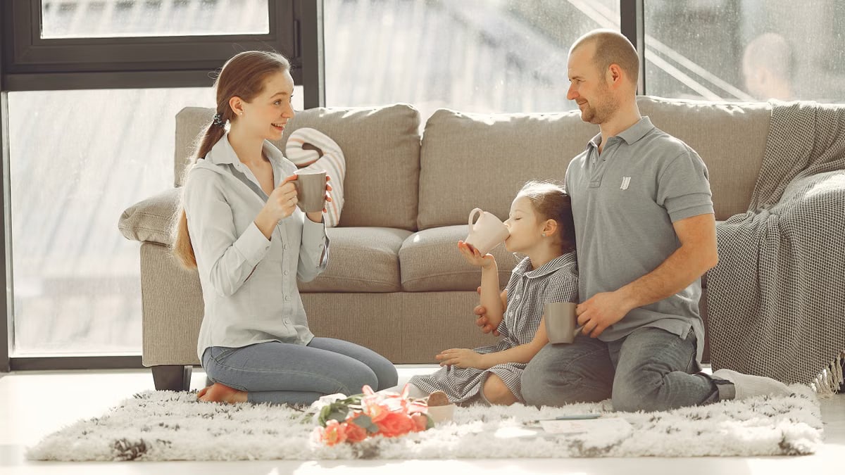Cheerful family drinking tea in living room while having rest and laughing together during weekend while spending time and having fun